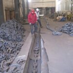 Workers checking and testing heavy anchor chain in factory workshop