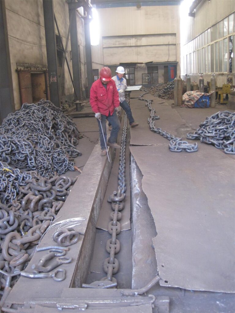 Workers checking and testing heavy anchor chain in factory workshop