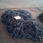 Black anchor chains arranged on workshop floor before shipment