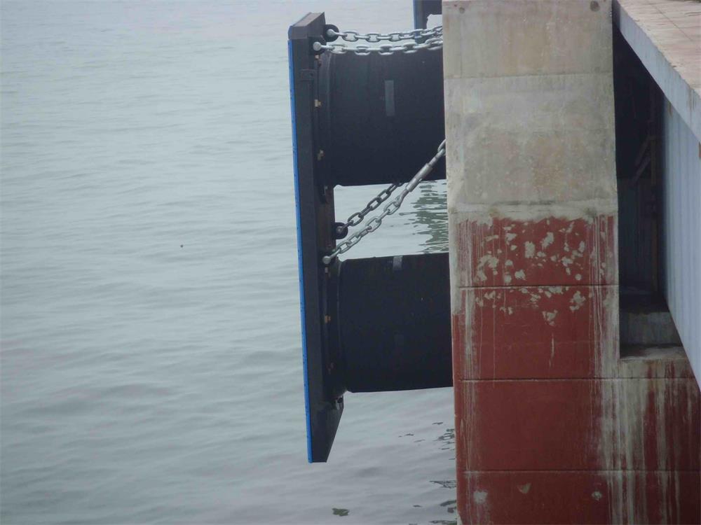 Fixed dock rubber fender with frontal panel and chains installed on a quay wall for berth protection