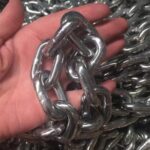 Workers checking and testing heavy anchor chain in factory workshop