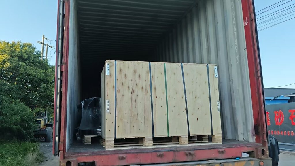 Strapped wooden crate and wrapped bollard inside an open shipping container at the factory