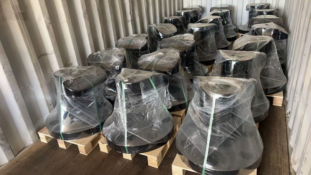 Black mooring bollards wrapped in clear film and strapped to wooden pallets inside a container